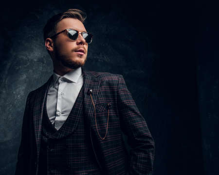 A confident elegantly dressed young man in sunglasses posing against a dark textured wallの写真素材