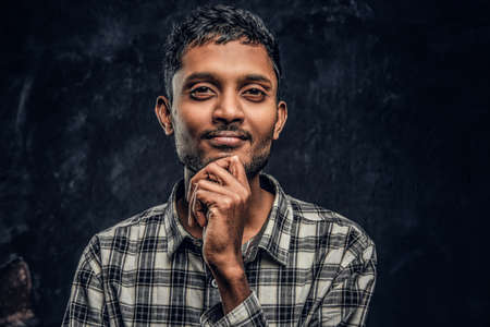 Close-up portrait of a handsome young Indian guy wearing a checkered shirt holding hand on chin and...