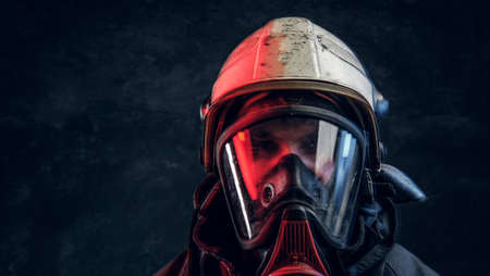 Brutal fireman in gas mask and helmet looks into camera on black background in studioの写真素材