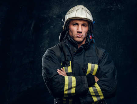Portrait of a fireman in uniform and helmet stands with crossed arms, looks at the camera with a...