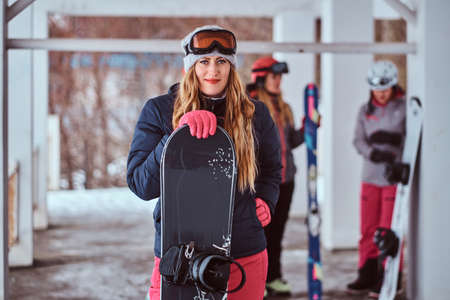 Charming Norwegian woman wearing warm clothes and goggles posing with a snowboard in the winter ski resortの写真素材