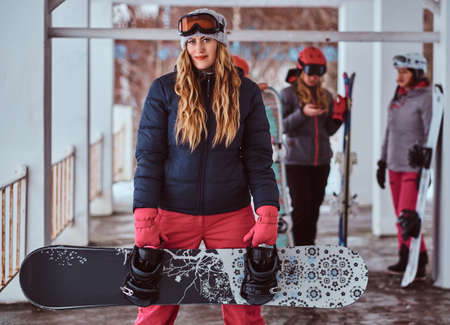 Charming Norwegian woman wearing warm clothes and goggles posing with a snowboard in the winter ski resortの写真素材