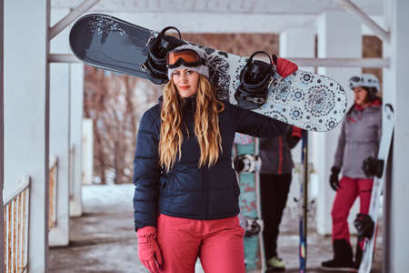 Charming Norwegian woman wearing warm clothes and goggles posing with a snowboard in the winter ski resortの写真素材