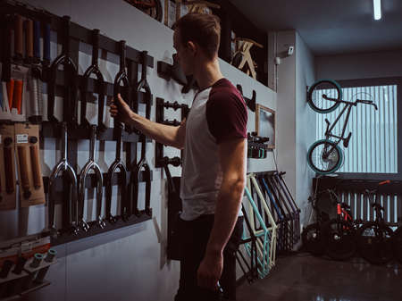 Young man holding a bicycle frame and choosing parts for his BMX in a shopの写真素材