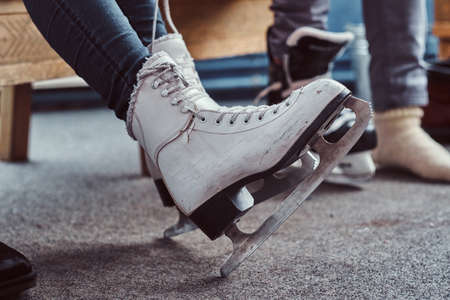 Young couple preparing to a skating. Close-up photo of their hands tying shoelaces of ice hockey skates in a locker roomの写真素材