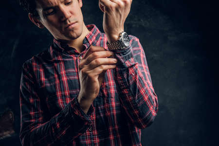 Concentrated young man tries to button on a shirt sleeve in a studio against the background of the...