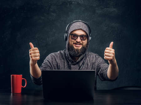 Satisfied hacker sits behind a laptop in a dark office