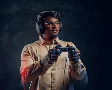 Indian man in wireless headphones holding joystick and plays video games on console standing in the...