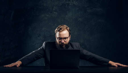 The bearded boss of the corporation looks into his laptop with spreaded arms to the side in the...