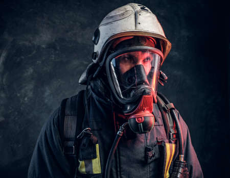 Close-up portrait of a firefighter in safety helmet and oxygen mask. Studio photo against a dark textured wallの写真素材