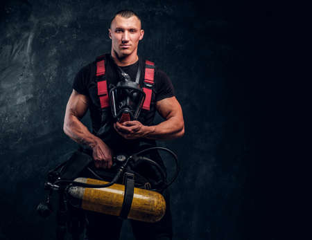 Portrait of a firefighter man holding an oxygen tank and mask, looking at a camera. Studio photo...