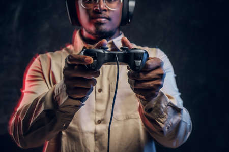 Cropped photo of a dark-skinned player with headphones and a game joystick on a black background in the studioの写真素材