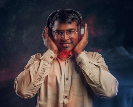 Young dark-skinned guy listens to music in headphones, smiles and looks at the camera in the studio on a black backgroundの写真素材