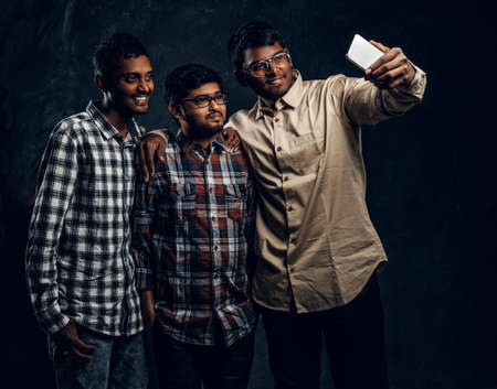 Three black-skinned friend in shirts smiling and posing standing for selfie in the studio on a black photoの写真素材