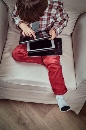 Top view of a young Caucasian schoolboy wearing a checkered shirt with tie using a digital tablet sitting on a couch at homeの写真素材
