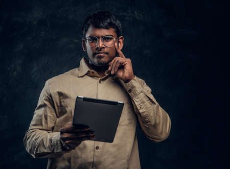 Young dark-skinned businessman holding a tablet in his hand and looking into the camera in the studio on a black backgroundの写真素材