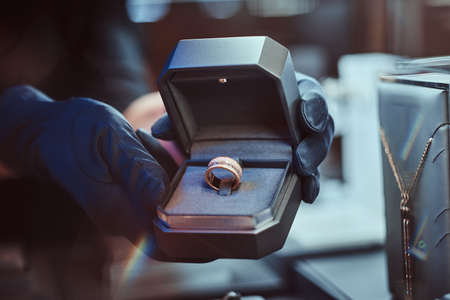 Close-up photo of assistants hands who holds the box with the exclusive gold ring in a luxury...