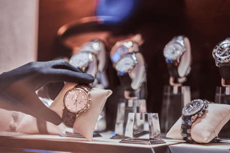 Close-up of the sellers hand in gloves shows the exclusive mens watch from the new collection in the luxury jewelry storeの写真素材