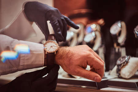Assistant helps the client to try on exclusive mens watches, close-up hands.