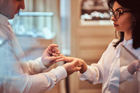 Elegantly dressed man trying on the wedding ring on the hand of his girlfriend in a luxury jewelry storeの写真素材