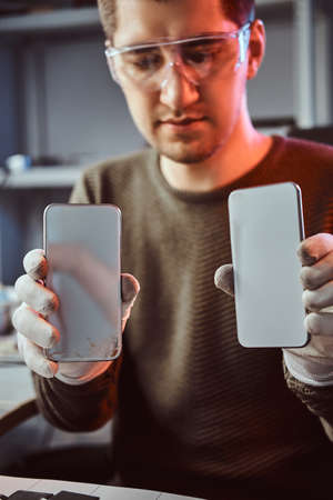 Electronic technician holds two identical smartphones for comparison, in one hand broken and in another newの写真素材
