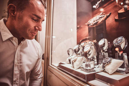 Handsome man looking at a showcase with an exclusive mens watches in a luxury jewelry storeの写真素材