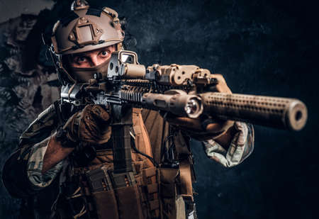 Close-up studio photo. Elite unit, special forces soldier in camouflage uniform holding an assault rifle with a laser sight and aims at the target.の写真素材