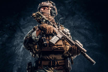 Elite unit, special forces soldier in camouflage uniform posing with assault rifle. Studio photo against a dark textured wallの写真素材