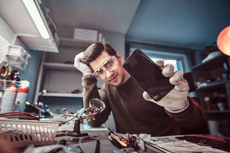 Electronic technician showing a modern smartphone with a broken body in a repair shopの写真素材