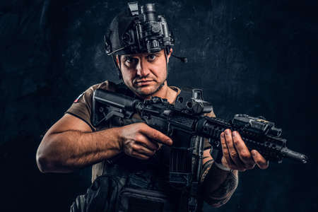 Brutal soldier of the Russian Federation wearing body armor and helmet with a night vision posing with an assault rifle. Studio photo against a dark textured wallの写真素材