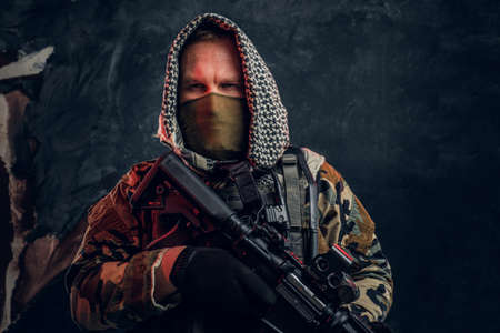 Close-up portrait of a Special forces soldier in military uniform wearing mask and hood Studio photo against a dark textured wallの写真素材