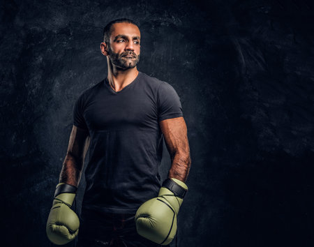 Portrait of a brutal professional fighter in a black shirt and gloves looking sideways. Studio photo...