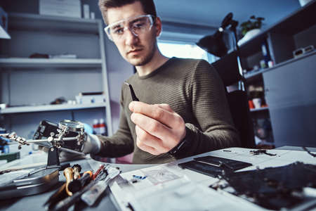 Electronic technician mending a broken phone, looking closely at the little bolt holding it with...
