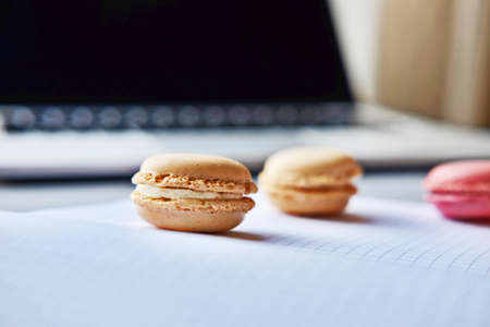 Open laptop, tablet, smartphone, notebook and colorful French macaron on a table. Work, lunch,...