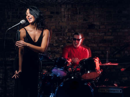 Jazz band performance. Young couple of musicians - a drummer and a singer in a nightclub.の写真素材