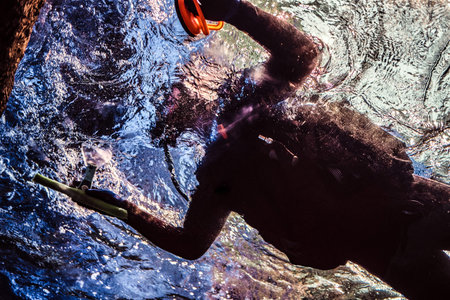 Bottom view of a diver floating near the surface of the water next to the rocky shore