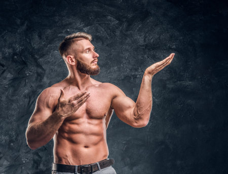 Male model with the muscular body posing for a camera. Studio photo against dark wall background