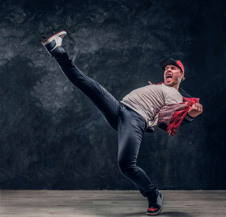Emotional stylish dressed man performing break dance moves on the floor. Studio photo against a dark textured wallの写真素材