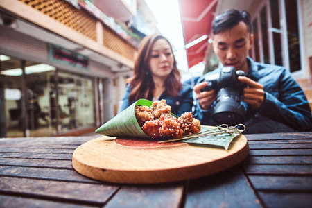 Young asian couple sitting in chinese restoraunt outside. At front on wooden table located traditional asian food - bamboo leaf wrap. People are watching pictures on camera. Widescreen shooting.の写真素材