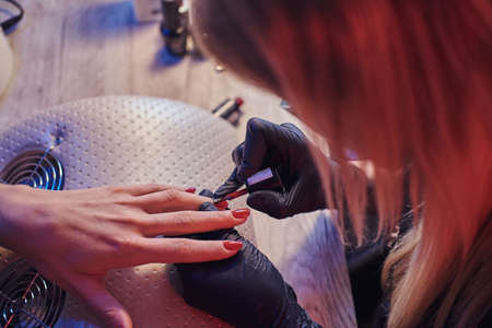Top view of a beautician master applying polish on clients natural nails at the manicure table in the beauty salon. Photo with dim light and red Blue backlightの写真素材