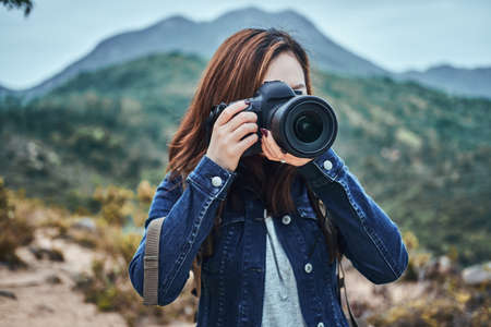 Nature photographer with digital camera is taking a photo shoot of nature. She has denim shirt.の写真素材
