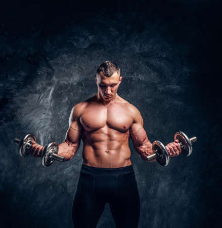Shirtless  muscular bodybilder is holding dumbbells. He is focused on  his exercise with closed eyes. There are dark background.の写真素材