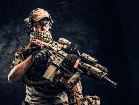 Special forces soldier in protective uniform holding an assault rifle. Studio photo against a dark textured wallの写真素材