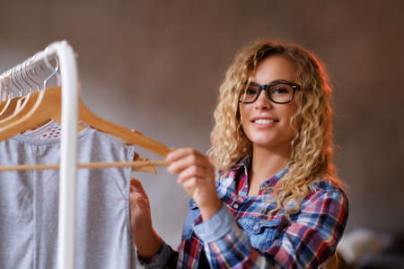 Smiling happy woman in glasses and checkered shirt chooses clothes for her holidays. She has blond curly hair. Woman is looking to the camera.の写真素材