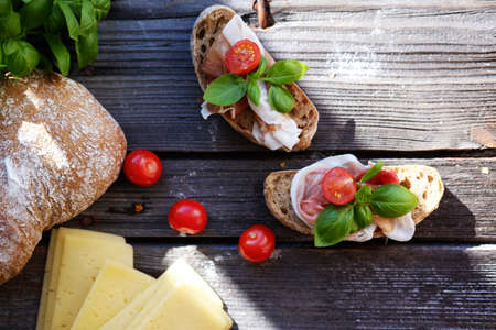 Delicious small sandwiches with meat, cherry tomatoes, cheese, bread and basil on the black table.