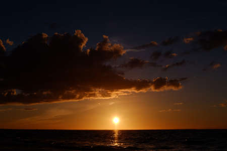 Dark sunset in with sun, sea, clouds and orange tones.