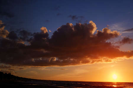 Dark sunset in with sun, sea, clouds and orange tones.の写真素材