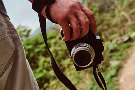 Man is holding camera in his hand while walking by the path throw the green mountains.