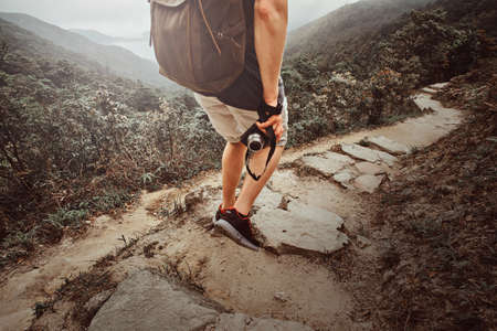 Man with backpack and camera is hiking by the stone path in the beautiful nature. There are fog and mountains at background.の写真素材
