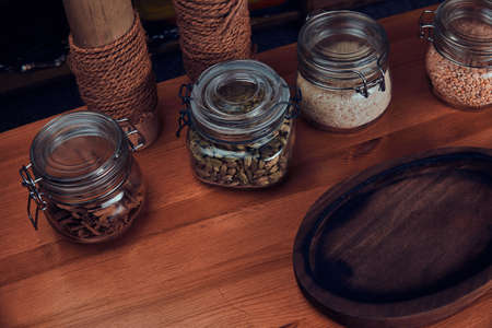 There are empty round wooden tray, cordamom, cinnamon bark, nuts and pepercorns in glass jars.の写真素材